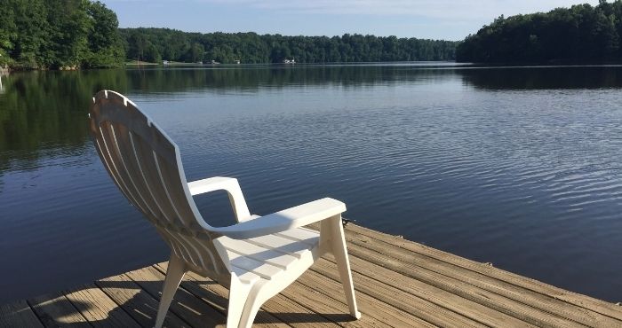 A white Adirondack chair sits on a dock facing the water